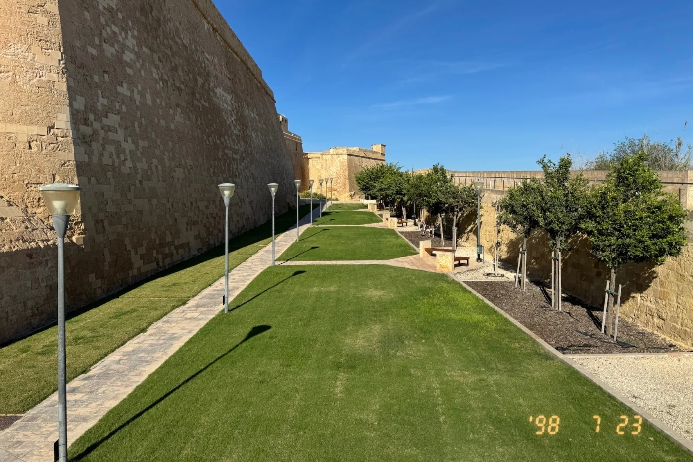 A photo of old fortress walls in Malta, stamped '98 7 23 in glowing orange digits